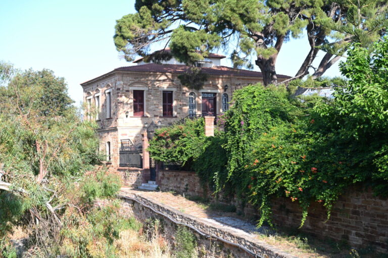 Panoramablick über die Kambos-Ebene mit sanften Hügeln, grünen Feldern und vereinzelten Häusern unter blauem Himmel.